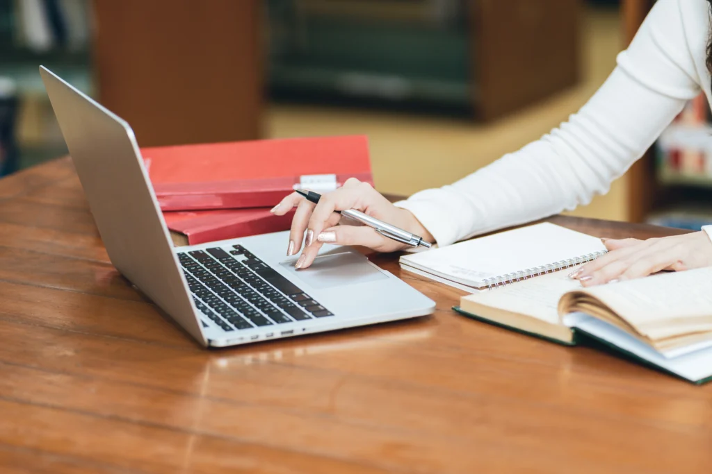 Manos femeninas usando laptop para investigación y redacción académica de trabajos como TFG y TFM.