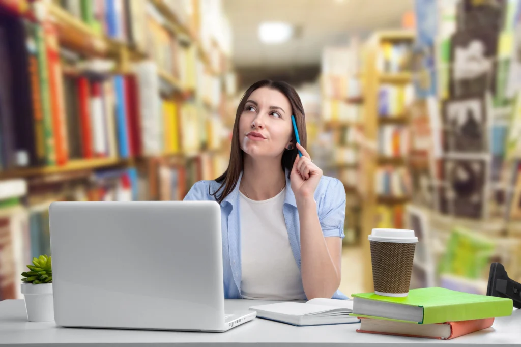 Estudiante pensativa con portátil y libros en una biblioteca.
